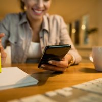 Close-up of woman using smart phone while learning in the evening at home.